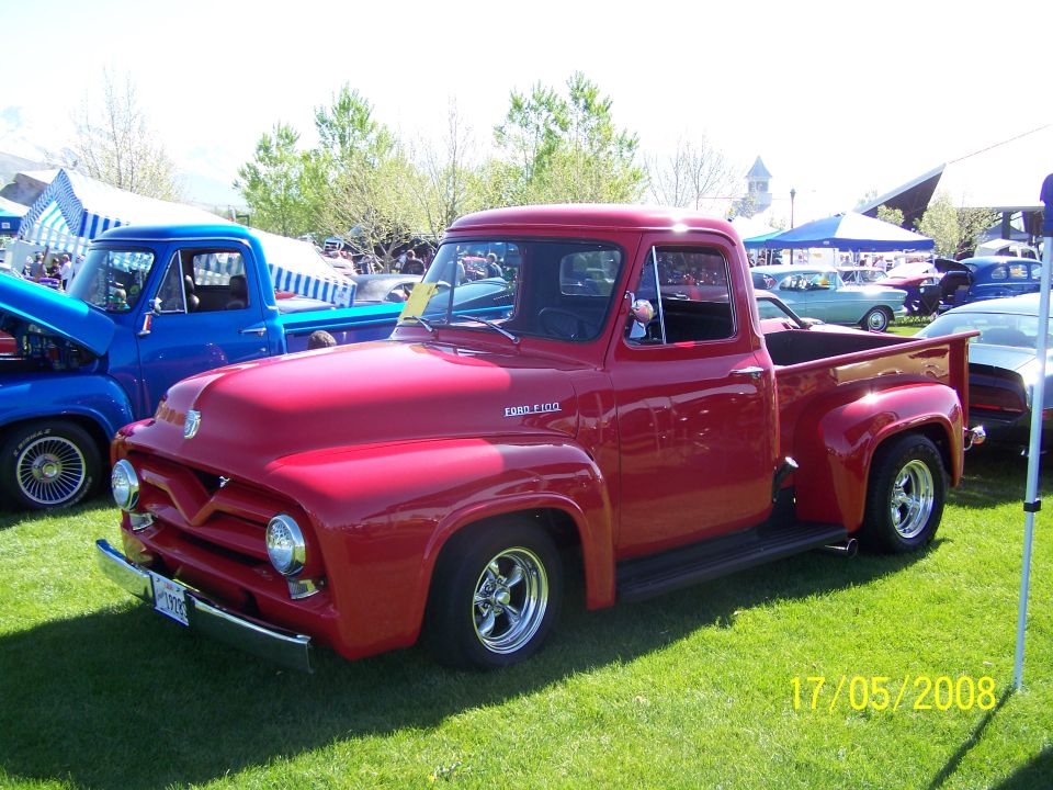 Red 1950s Ford F-100 pickup truck at an outdoor car show.