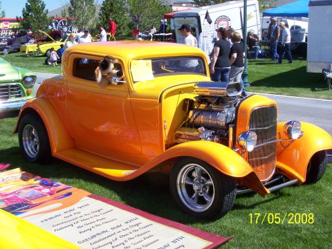 1973 Ford Mustang - A bright orange and yellow hot rod coupe with a dog looking out the driver's side window is parked on a grassy lawn. The car features a pro…