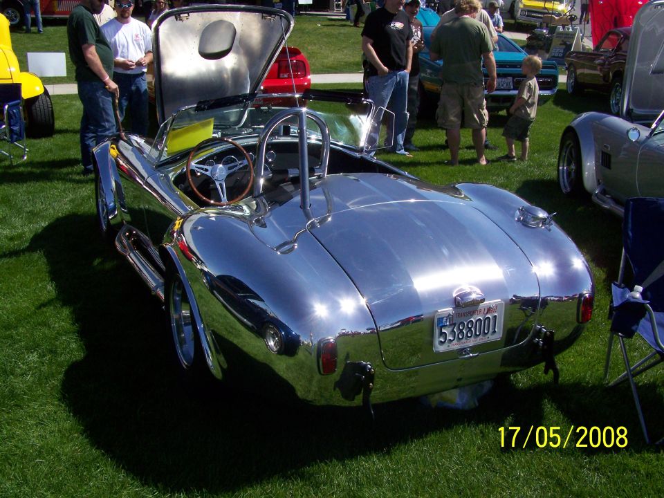 Chrome-finished 1960s style sports car with roll bar and wooden steering wheel.