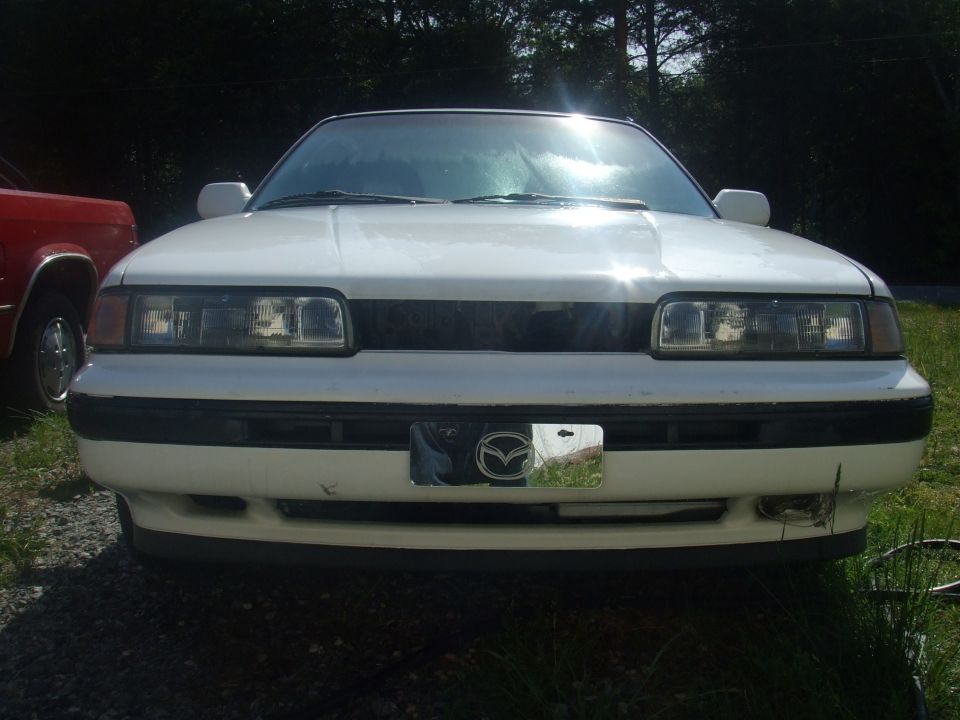 Front view of a white Mazda sedan with a Mazda logo license plate.
