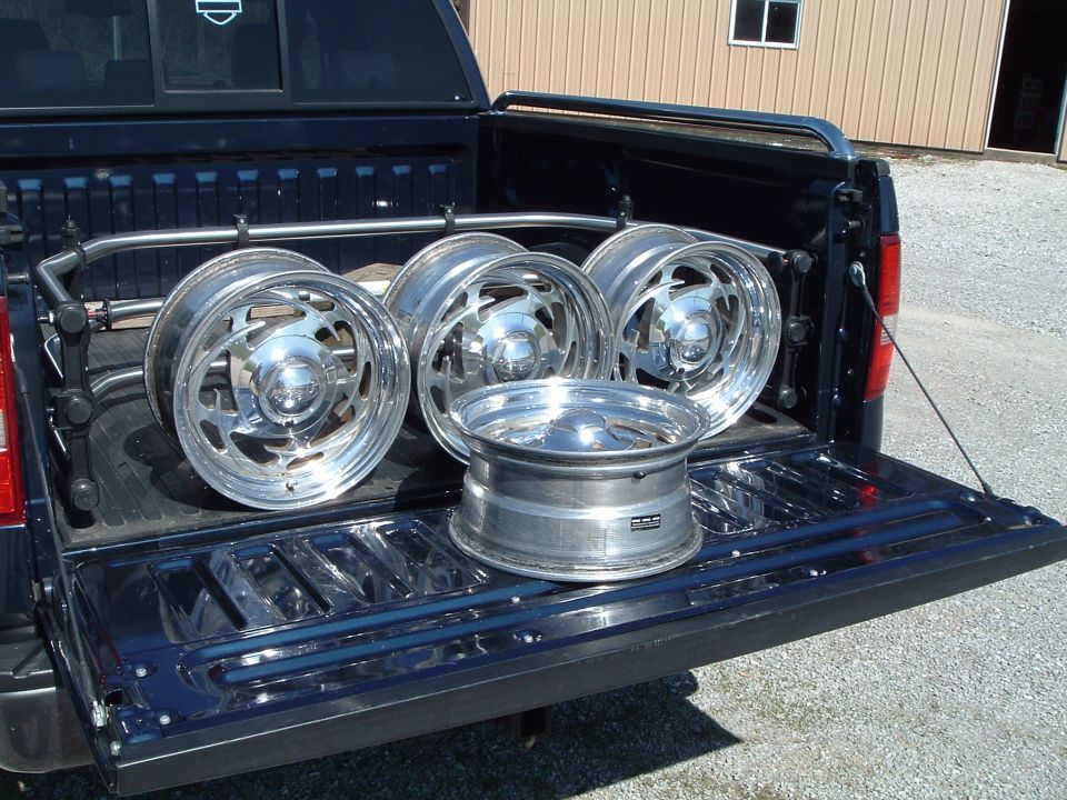 Four polished slotted alloy wheels in the bed of a dark blue pickup with tailgate down