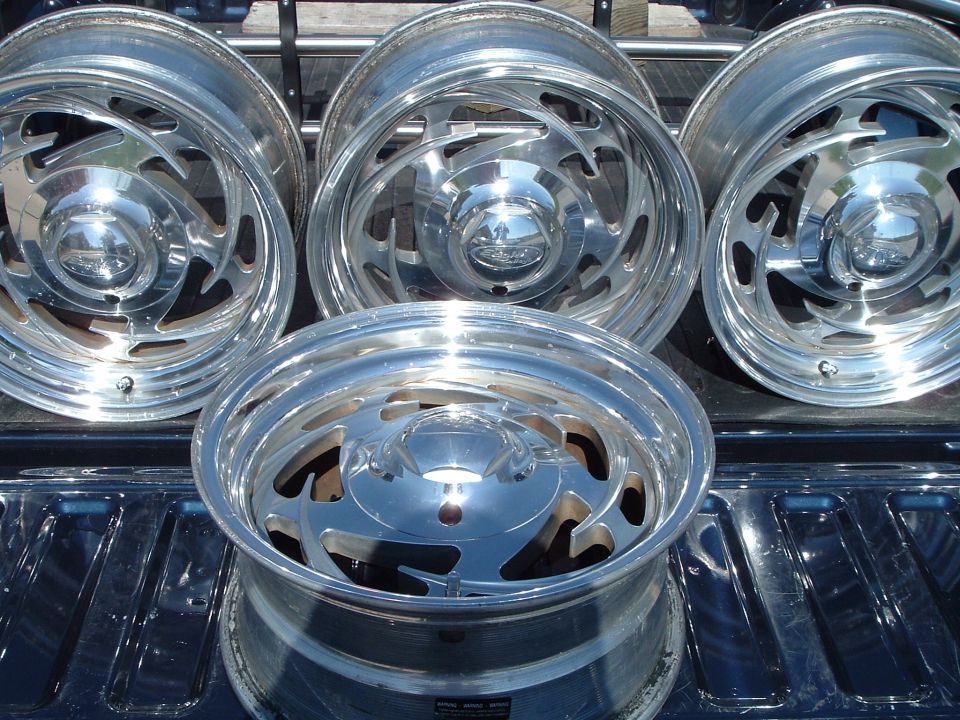 Four polished slotted alloy wheels staged in a black truck bed