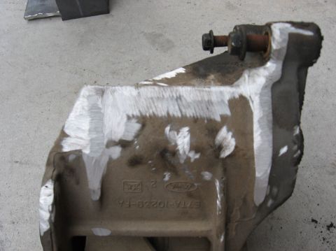1978 Ford Bronco - A removed cast/stamped Ford bracket sitting upside down on concrete, stamped with the Ford oval and part number E7TA-10229-FA, with a rusty…