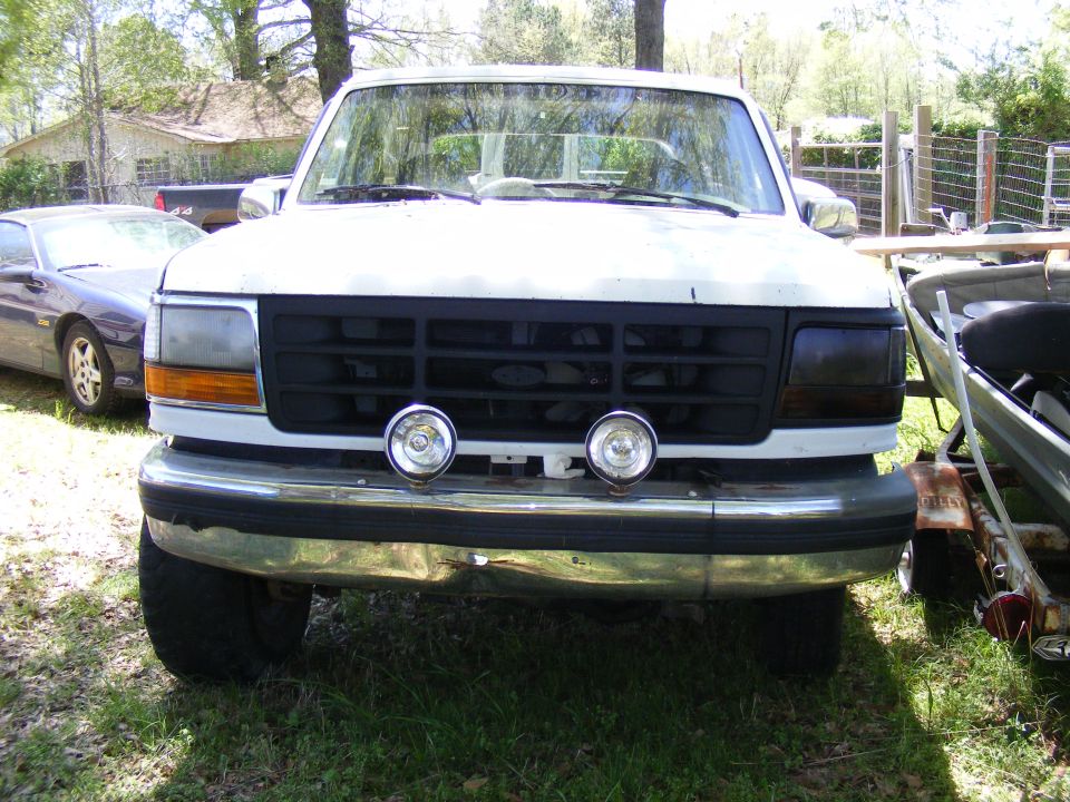 Front of white Ford truck/SUV with black grille and driving lights parked on grass