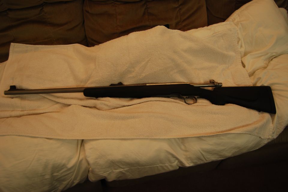 A rifle lying on a white towel on a couch.