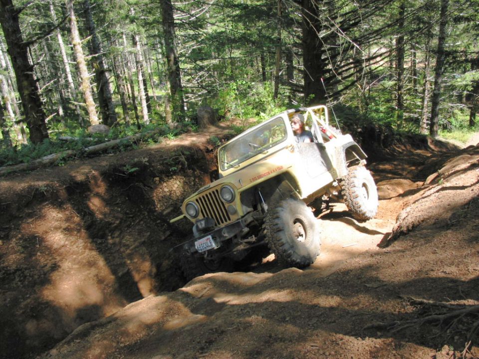Yellow Jeep Wrangler with large tires navigating a steep dirt incline