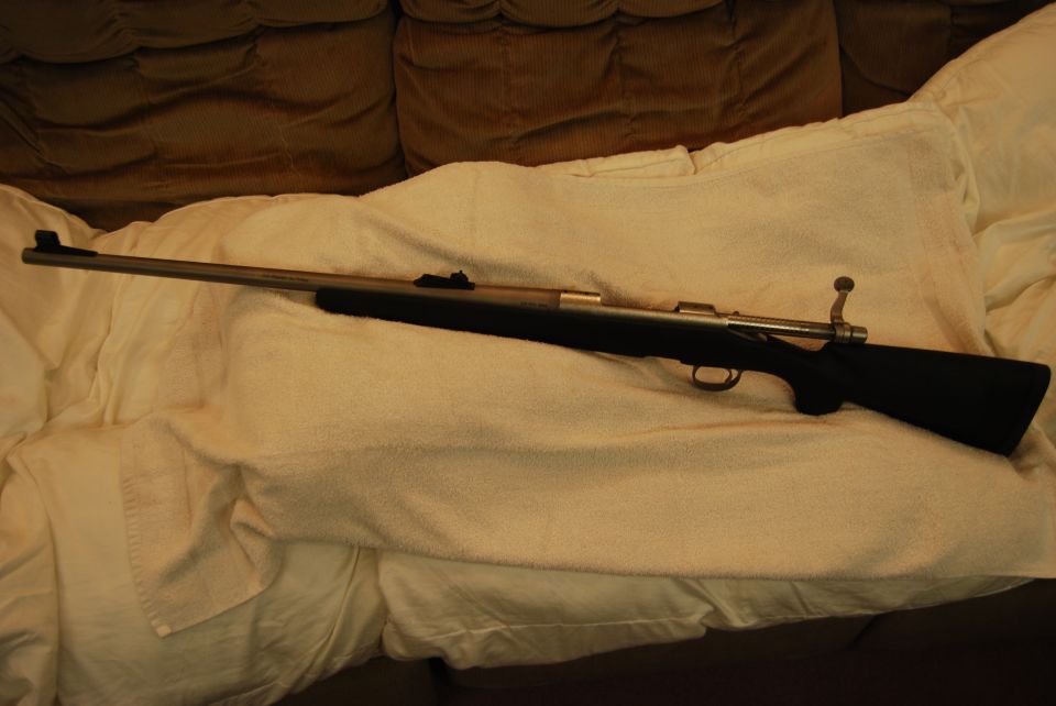 A rifle on a white towel on a couch.