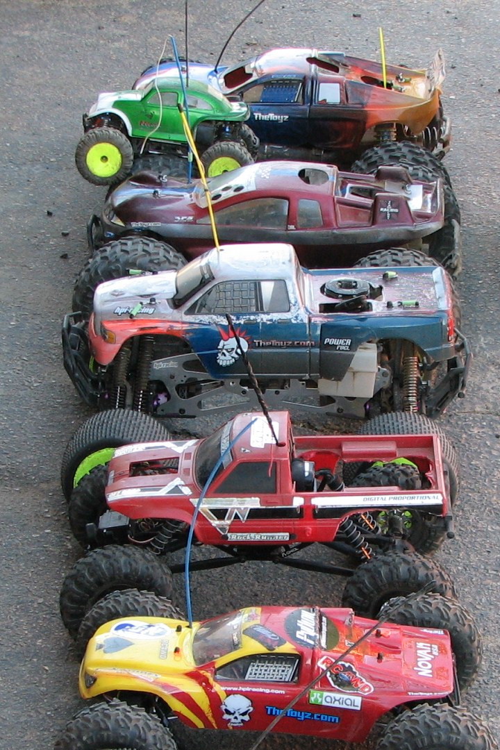 Five remote-control monster trucks parked in a line on asphalt.