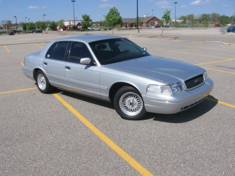 1988 Mercury Grand Marquis - A silver 2003-2011 Ford Crown Victoria sedan is parked in a paved parking lot with yellow lines. The car is viewed from the front three-qua…