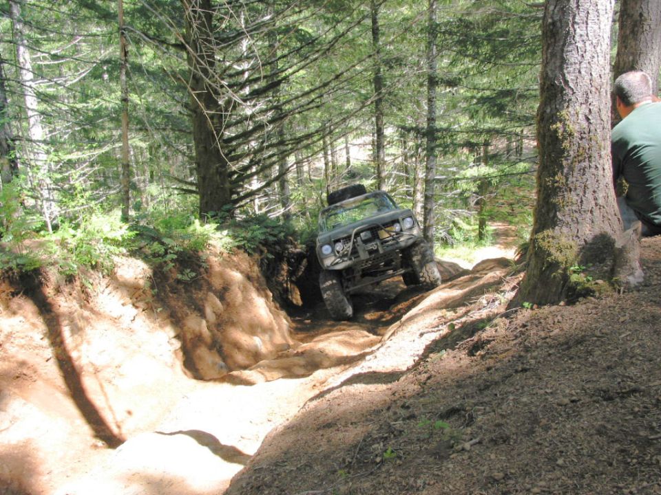 Green off-road vehicle with a roll cage navigating a steep dirt path in a forest