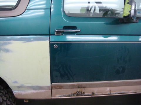1996 Ford Bronco - The door panel of a Ford Bronco shows signs of repair and rust on the lower trim piece.