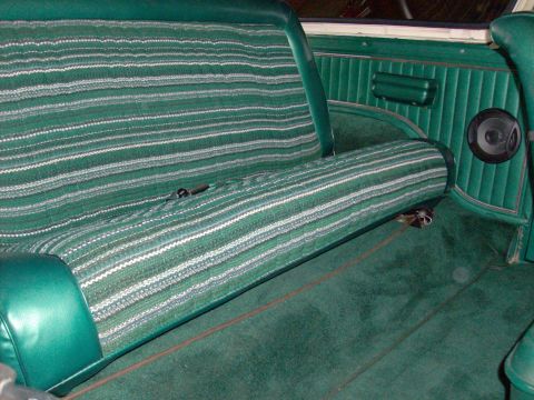 1978 Ford Bronco - The interior of a vehicle shows a green striped bench seat and matching carpet, with a speaker mounted on the door panel.