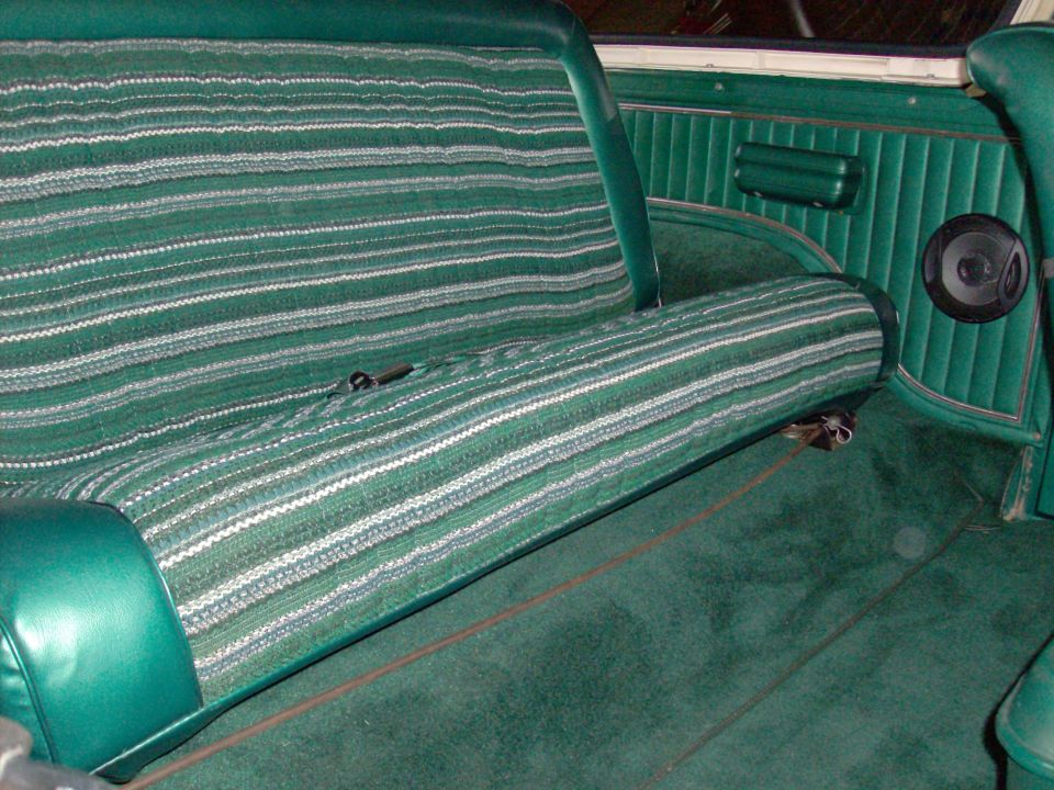 Green striped bench seat and carpet in a vehicle interior with a speaker visible on the door panel