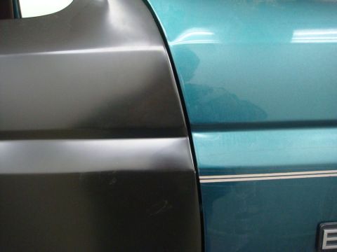 1996 Ford Bronco - Close-up of a car door panel, showing an unpainted section adjacent to a teal painted section with a stripe.