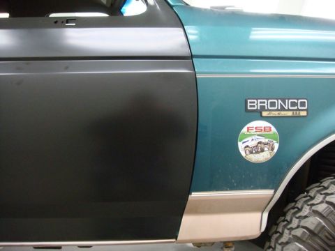 1996 Ford Bronco - A teal 1996 Ford Bronco door panel is shown with a black replacement panel and an Eddie Bauer badge.