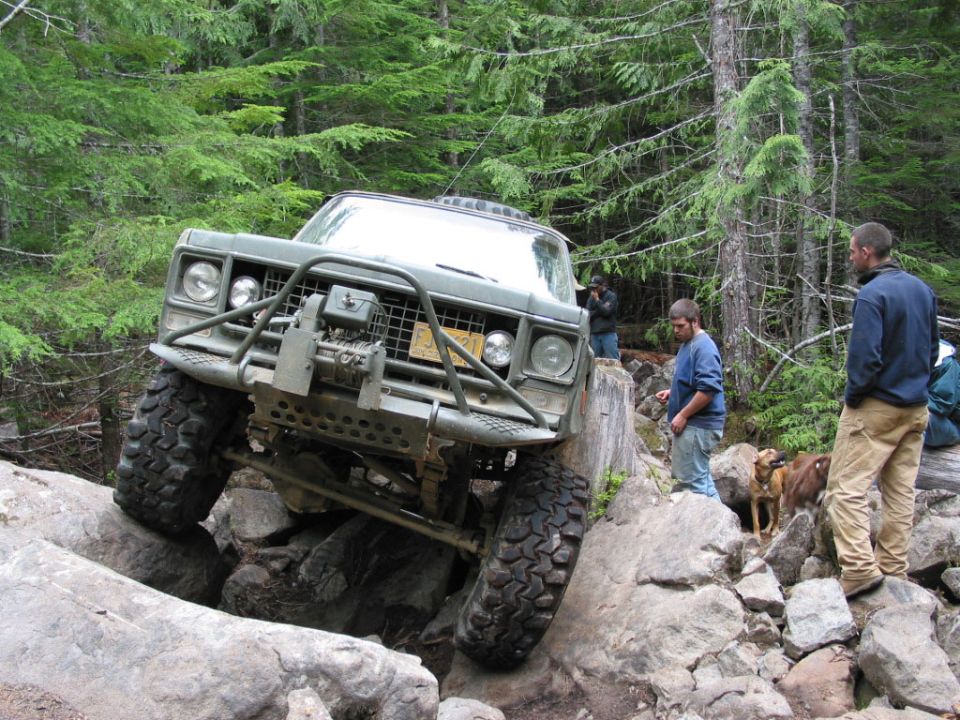 Off-road vehicle with winch and brush guard navigating large rocks in a forest