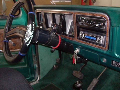 1978 Ford Bronco - The dashboard of a green truck features two radios and a steering wheel with a custom cover.