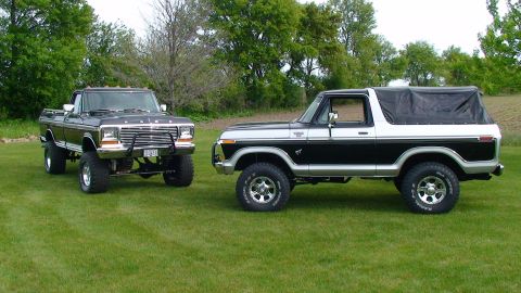 1979 Ford Bronco - Two classic Ford trucks, a pickup and a Bronco, are parked side-by-side on a grassy lawn.
