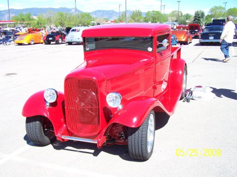 1972 Ford Ranchero - A bright red hot rod pickup truck is parked at a car show with other vehicles in the background.