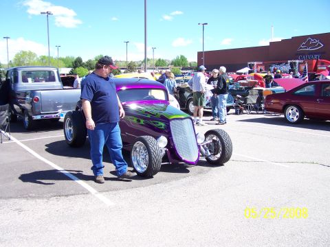 1972 Ford Ranchero - A man stands by a custom purple hot rod with green flame graphics at an outdoor car show.