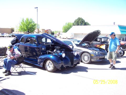 1972 Ford Ranchero - A blue hot rod sedan with its hood open is displayed at a car show, with other vehicles and people around.