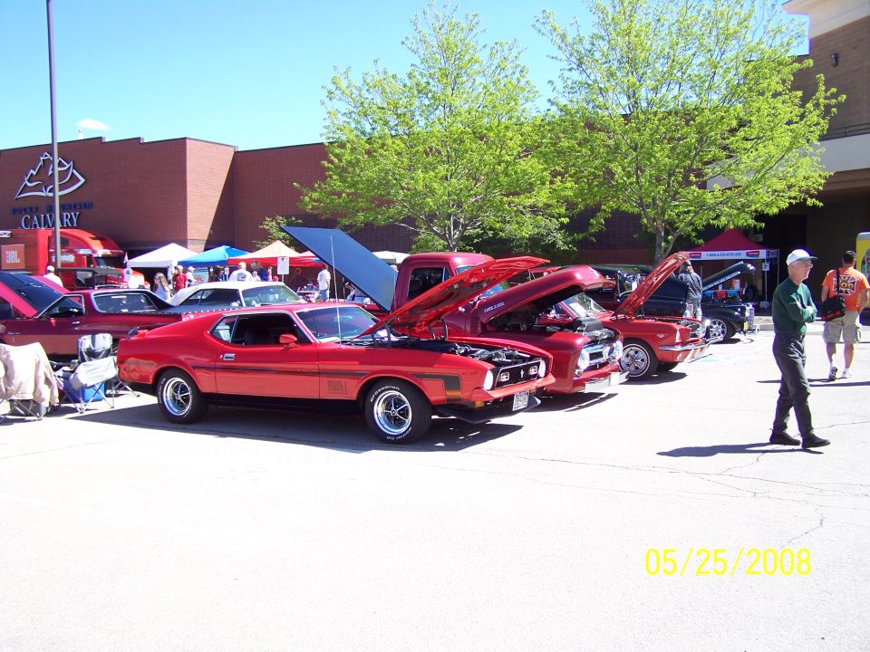 Red muscle car with black stripes and hood scoop at a car show