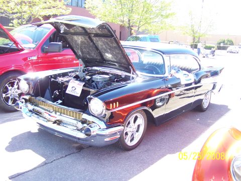 1972 Ford Ranchero - A classic black 1957 Chevrolet Bel Air is displayed with its hood open at a car show, alongside a red pickup truck.