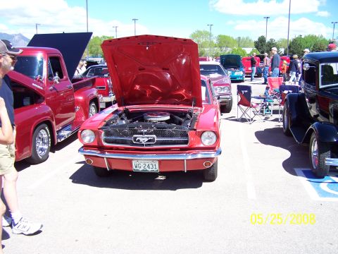 1972 Ford Ranchero - A red 1965 Ford Mustang is displayed with its hood open at a car show. Other vehicles are visible in the background.