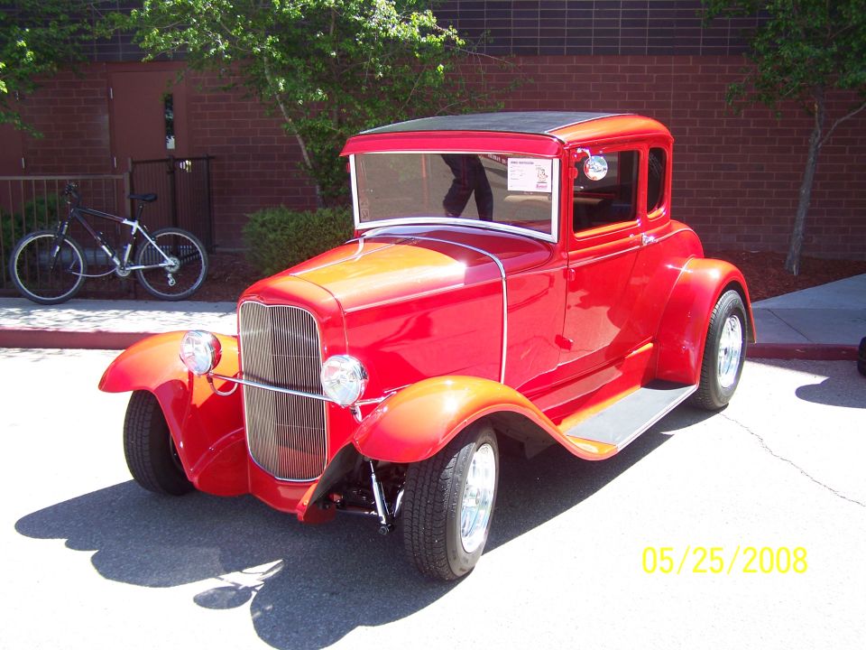 Red hot rod coupe with a black roof and chrome grille. A bicycle is parked behind it