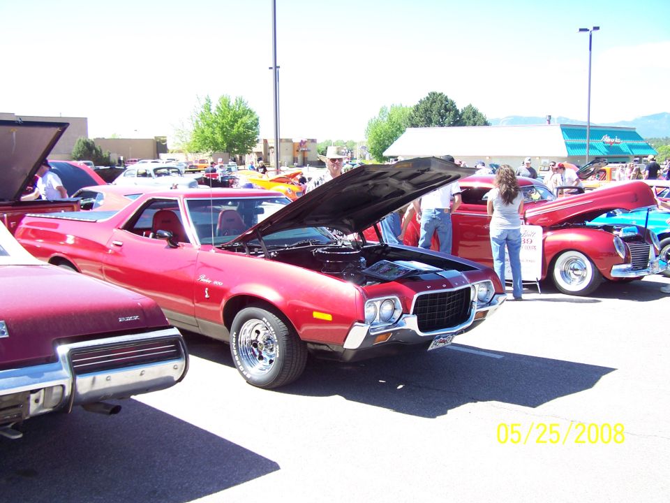 Red 1972 Ford Ranchero with hood open, parked at a car show. Chrome wheels and grille are visible