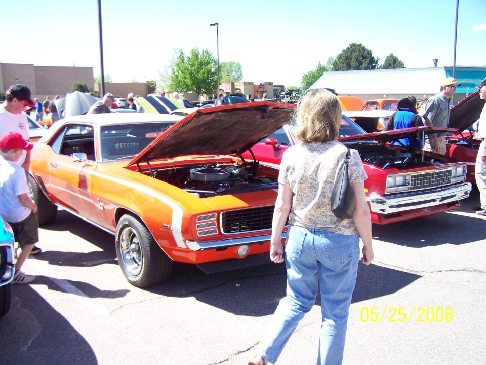 Orange 1969 Chevrolet Camaro with white stripes, hood open, parked at a car show