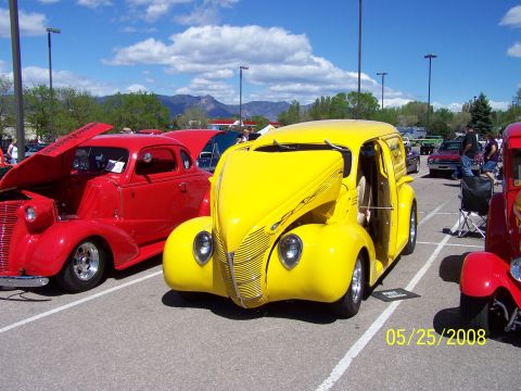 1972 Ford Ranchero - A bright yellow panel van is parked at a car show next to a red coupe.