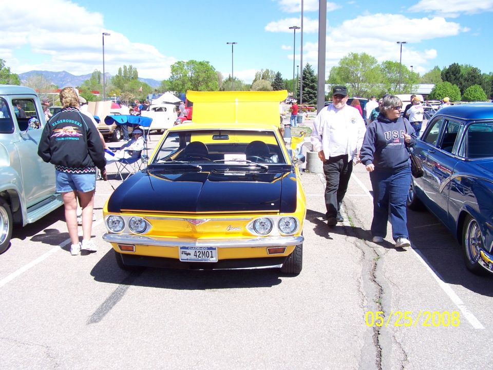 Front view of a yellow 1972 Chevrolet Corvair with a black hood, parked at a car show. License plate reads 42M01