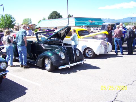 1972 Ford Ranchero - Two classic cars are on display at a car show, one dark green convertible and a white car with a yellow hood.