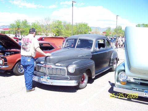 1972 Ford Ranchero - A dark gray 1940s Mercury sedan is parked at a car show, with other vehicles visible and a man looking at it.