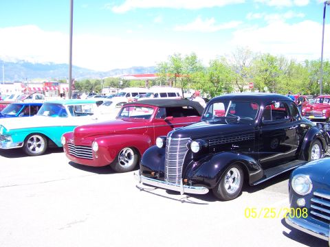 1972 Ford Ranchero - A line of classic cars is parked at an outdoor show, including a black coupe with a prominent chrome grille.