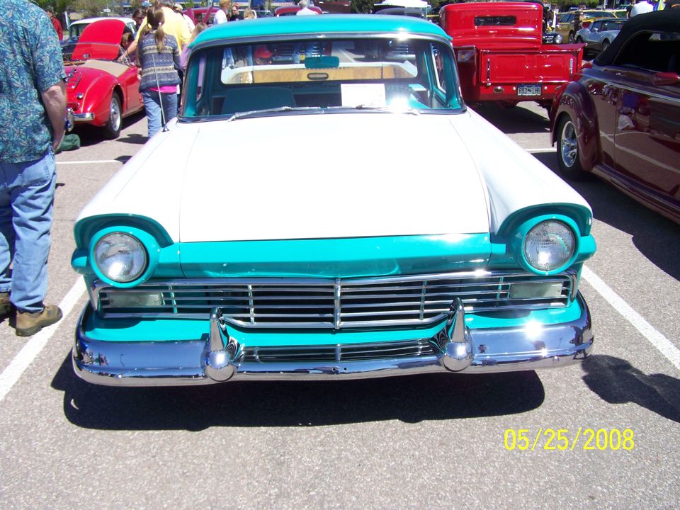 1957 Ford Fairlane 500 Skyliner front view, white and turquoise two-tone paint, chrome bumper and grille. Other cars visible in background