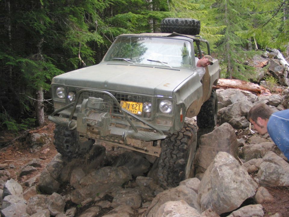 Green off-road truck with winch bumper crawling over boulders in the woods