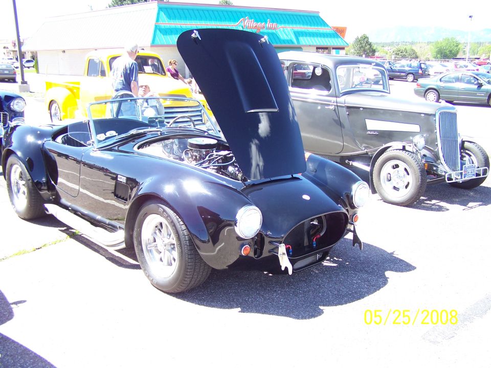 Black AC Cobra replica with hood open at an outdoor car show