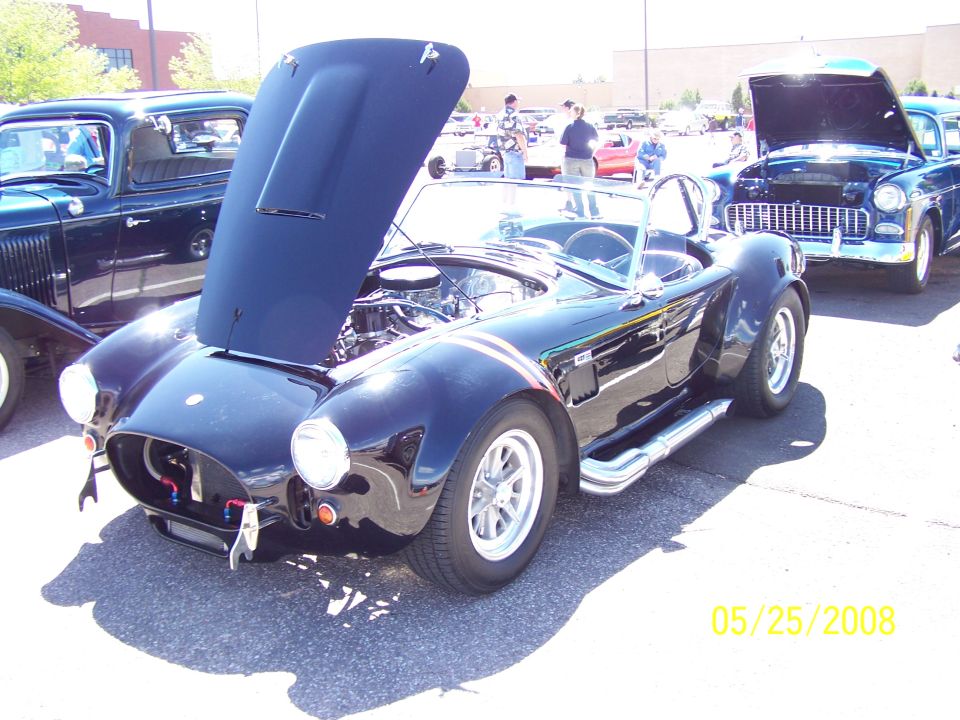 Black AC Cobra roadster with hood up at a car show
