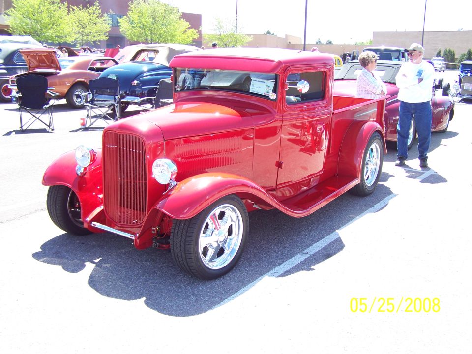 Red 1930s-style pickup truck with chrome grille and wheels at a car show.
