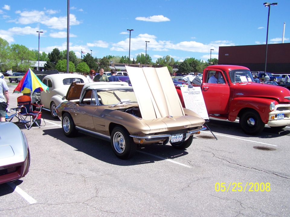 Gold 1964 Corvette Stingray convertible and a red 1950s pickup truck at a car show.
