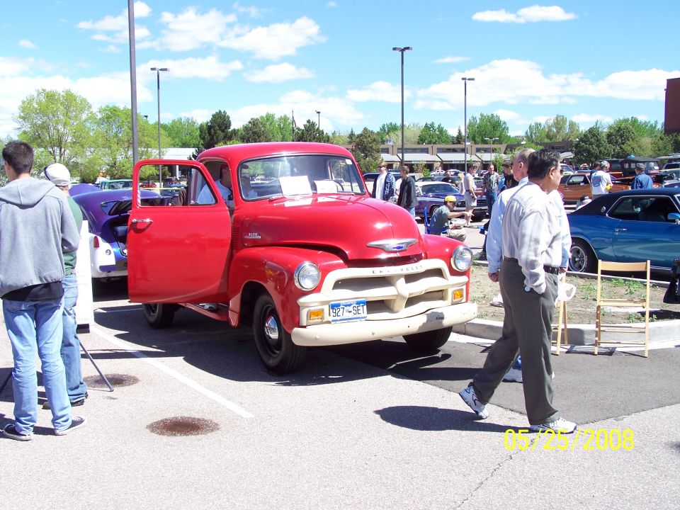 Red vintage Chevrolet pickup truck with driver's door open, parked at an outdoor event.