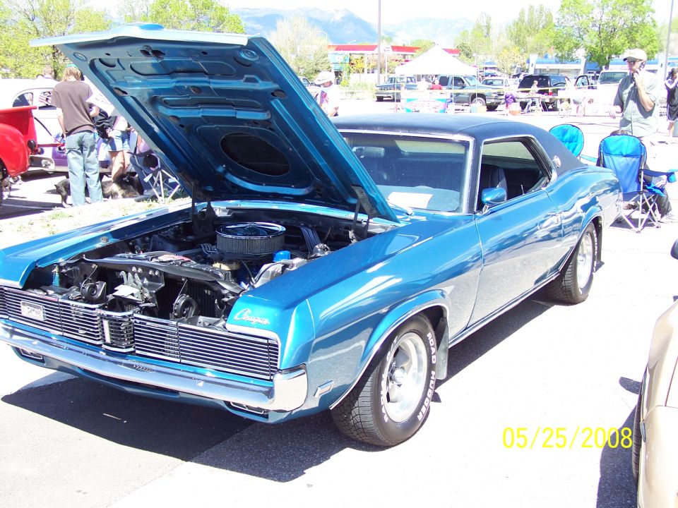 Blue 1970s coupe with hood open, showing engine, parked outdoors.