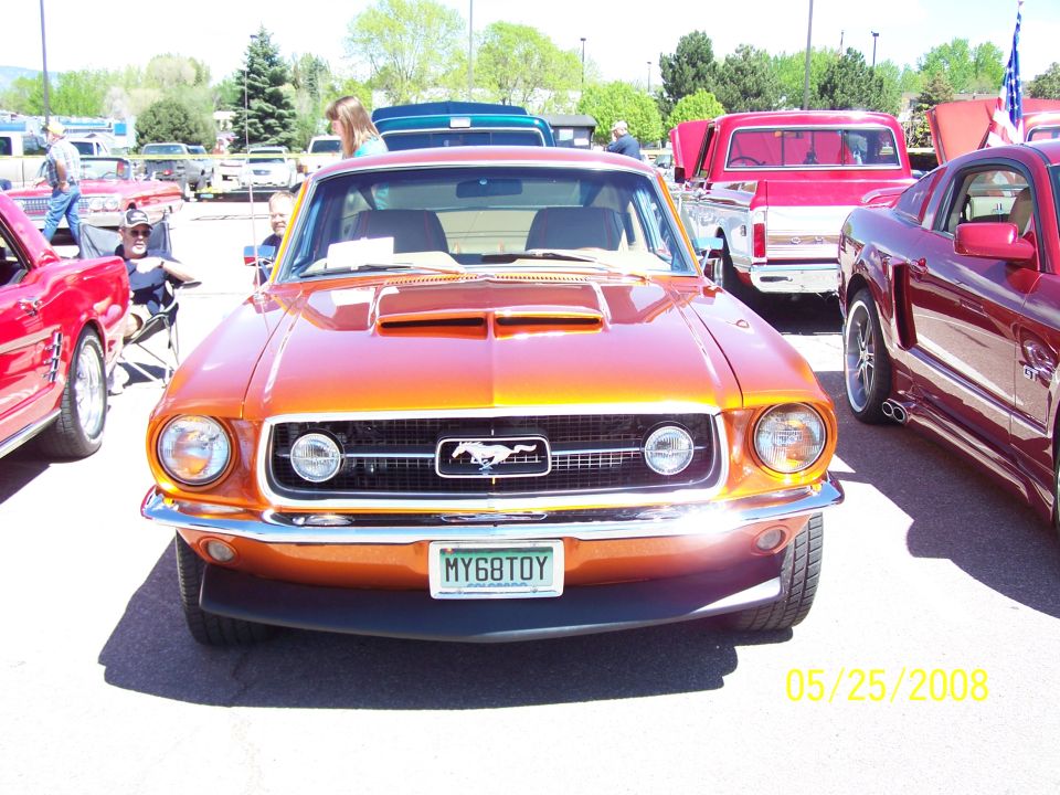 Orange Ford Mustang convertible with a white license plate, viewed from the front