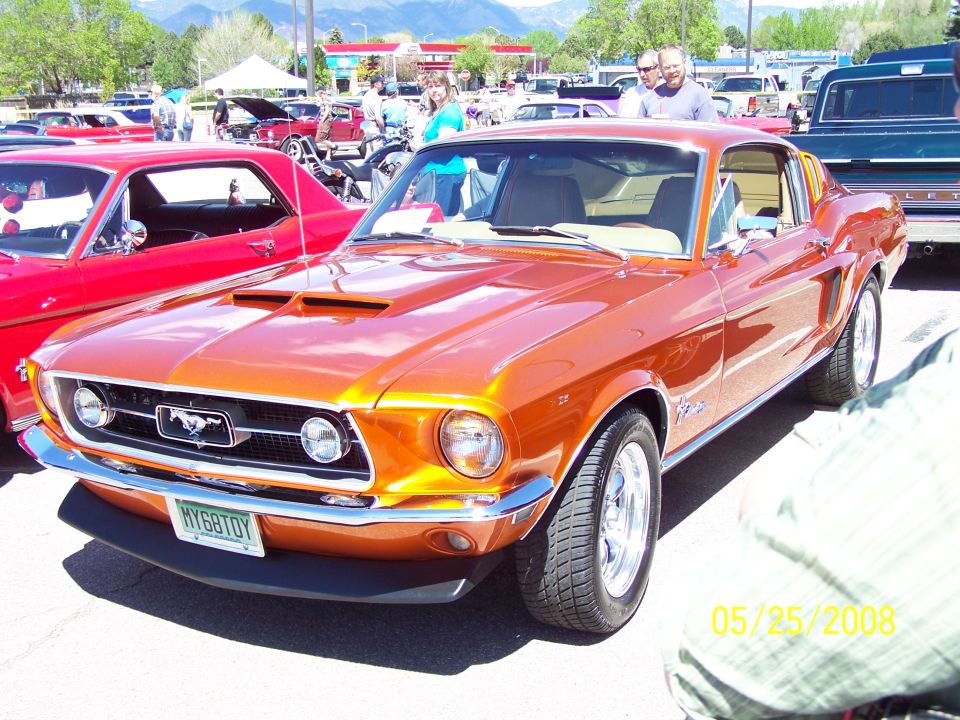 Orange 1967-1968 Ford Mustang coupe with custom hood scoop and chrome wheels.