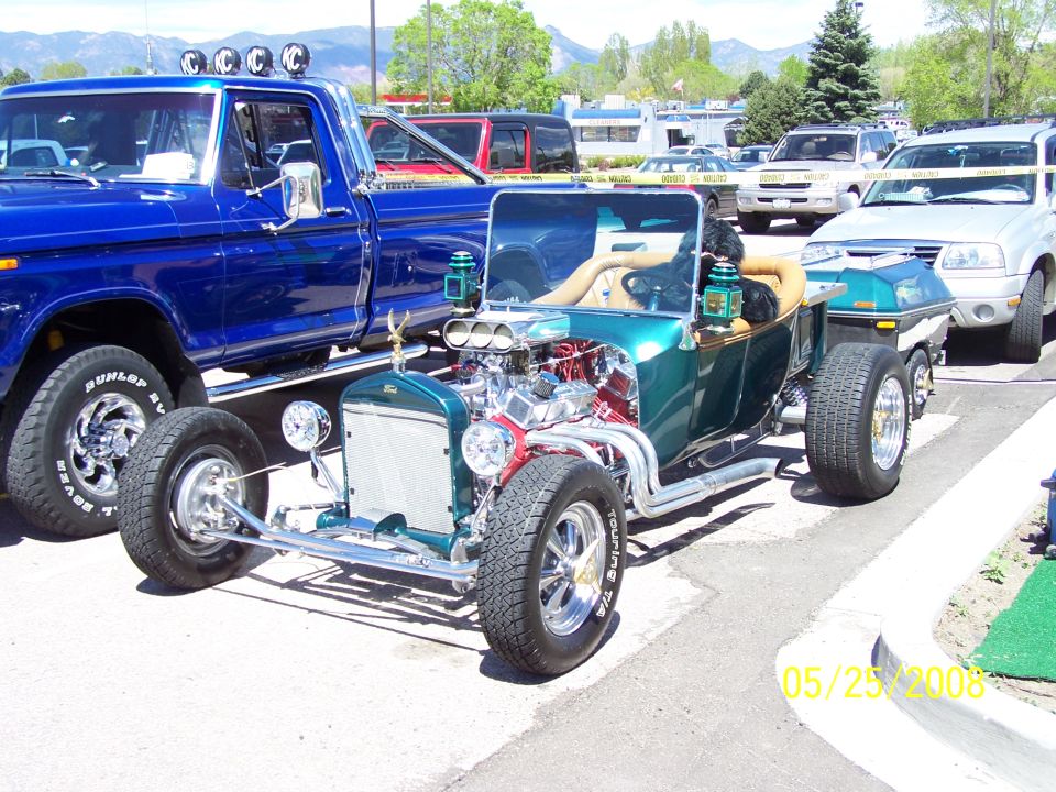 Green Ford Model T bucket hot rod with chrome engine beside a blue truck