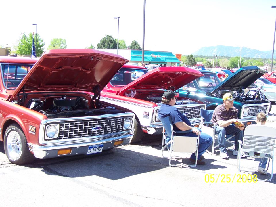 Two Chevrolet C10 pickups with hoods open and people seated at a car show
