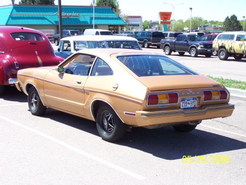 1972 Ford Ranchero - A gold Ford Mustang II is parked in a lot next to other vehicles, with a Village Inn in the background.