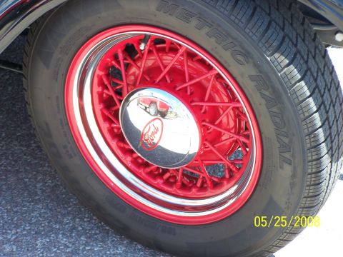 1972 Ford Ranchero - A close-up view of a red wire wheel with a chrome hubcap displaying the Ford logo, and a tire with visible text.